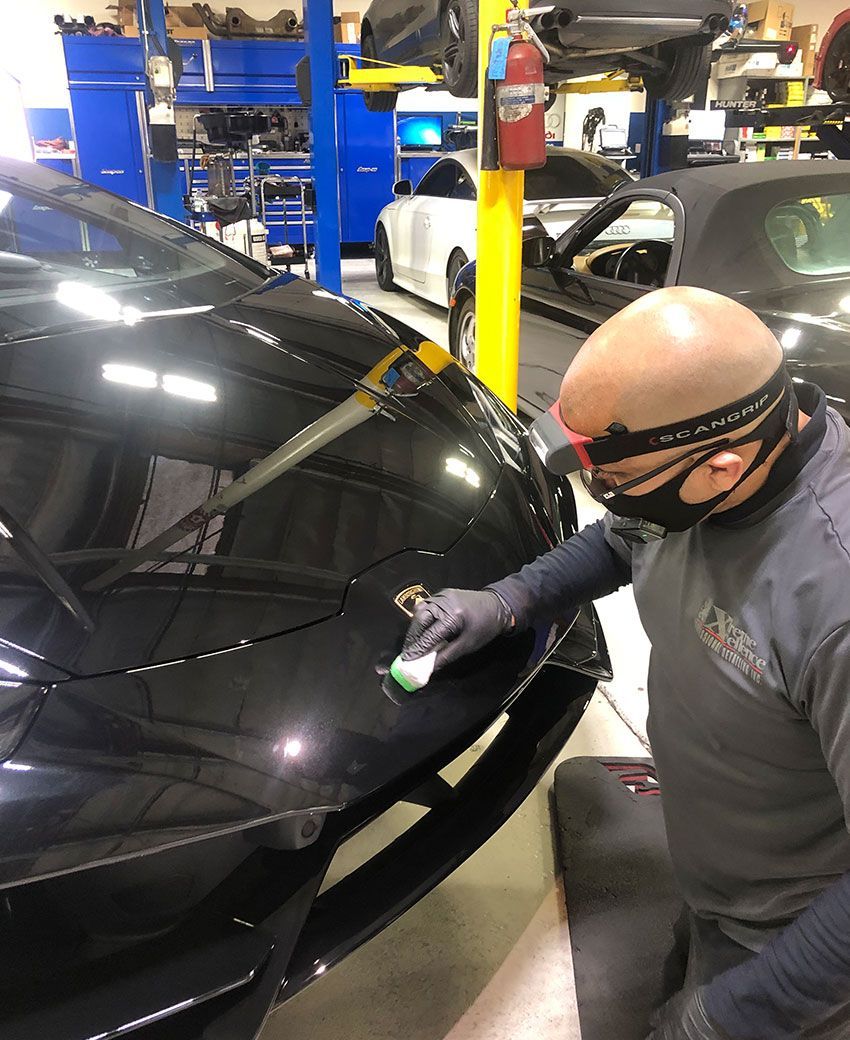 Ceramic coating service — dark sports car under IR curing lamps in the studio.