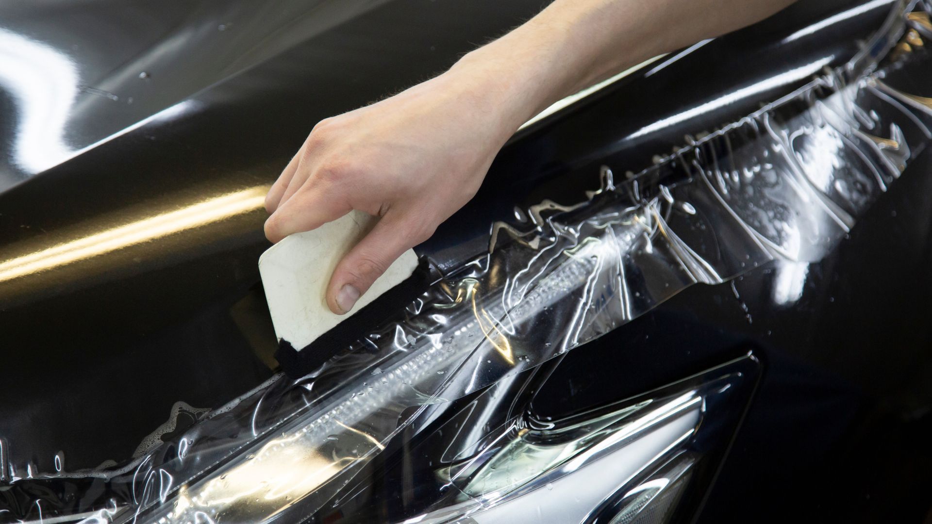 Paint Protection Film install — a black sedan with XPEL clear PPF being applied to the front end.
